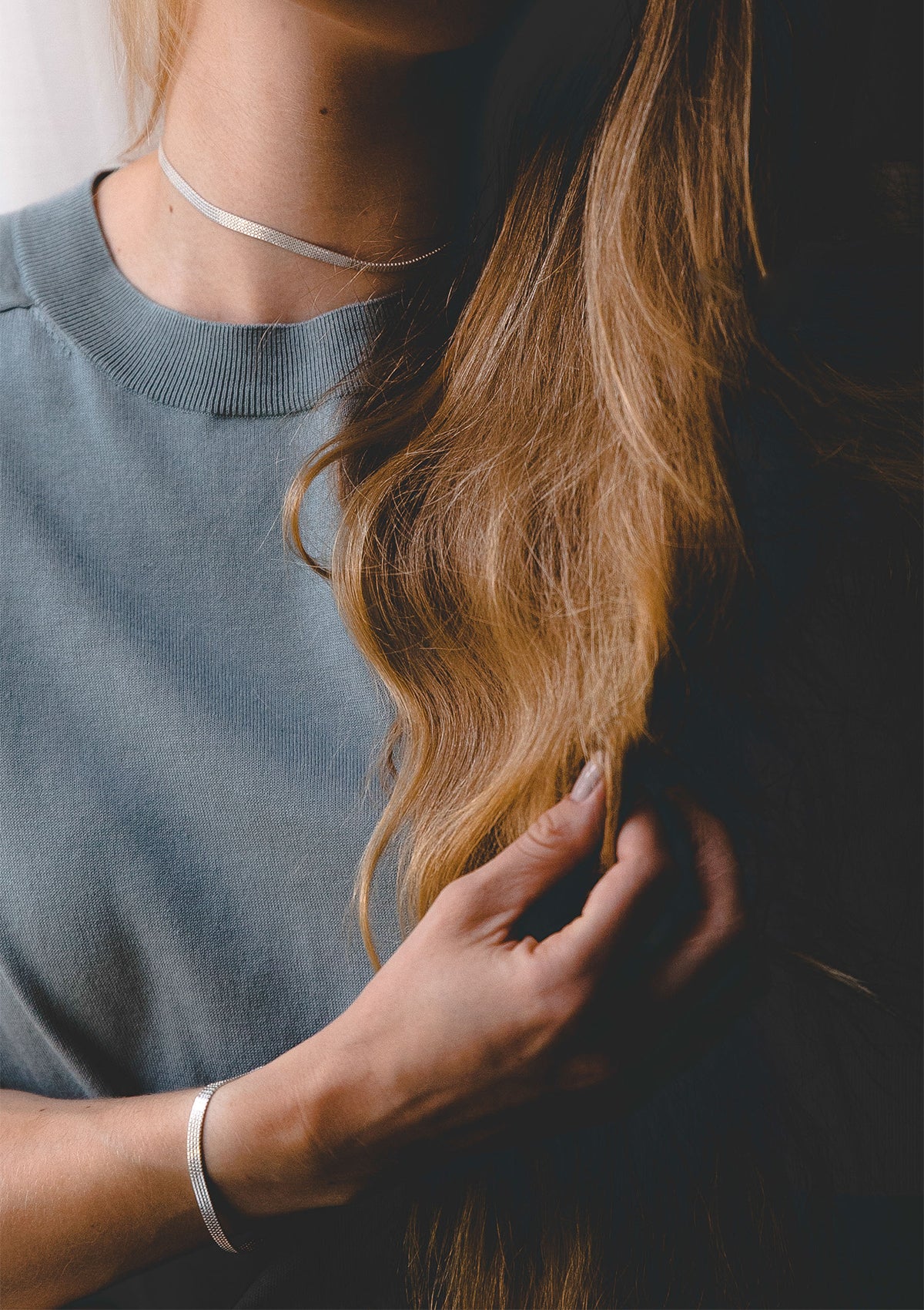Minimalist silver bracelet worn casually, shiny flat link chain peeking as model holds hair, everyday styling detail