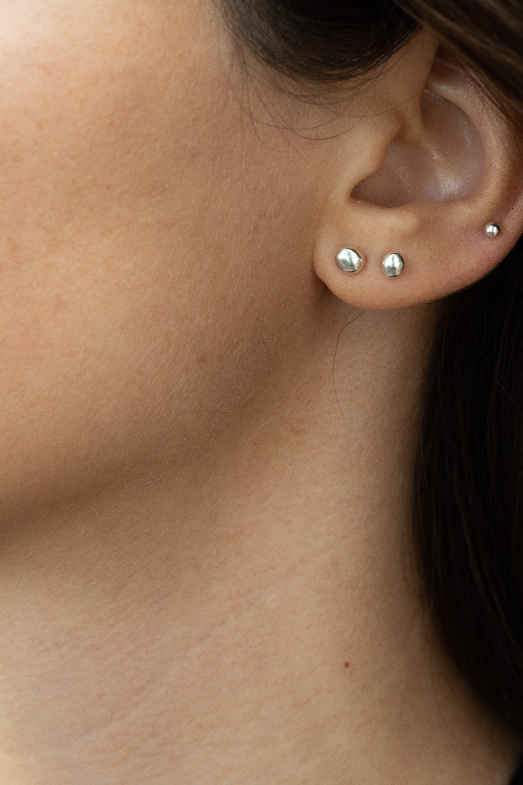 Organic grain-shaped silver earrings worn as mismatched studs, subtle sparkle shown on earlobe