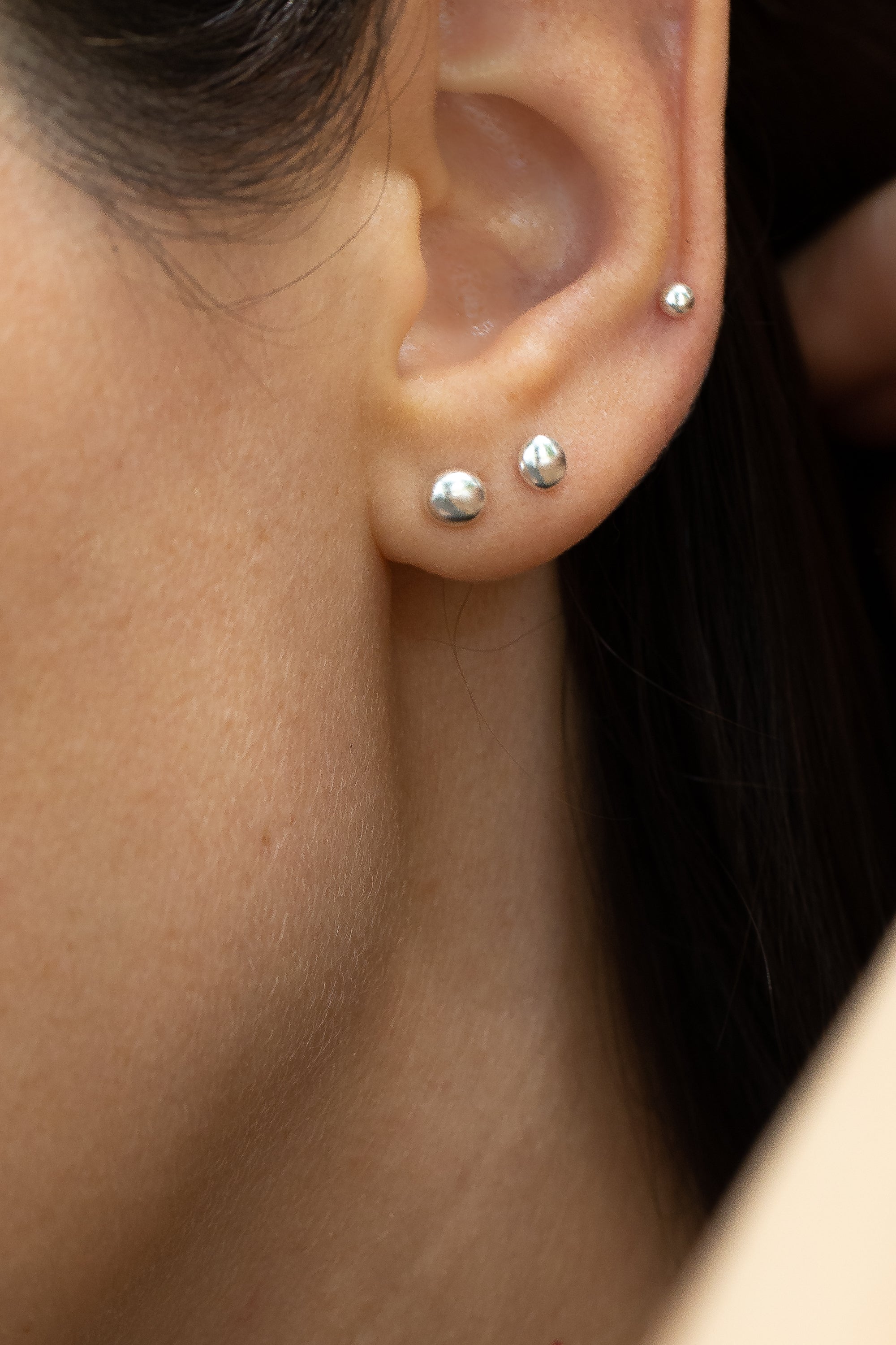 Organic grain-shaped silver earrings worn as mismatched studs, subtle sparkle shown on earlobe