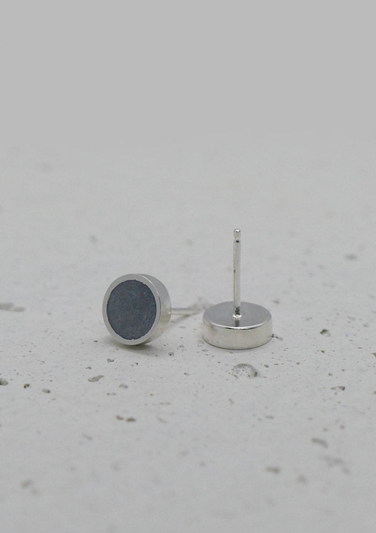 Minimalist sterling silver earrings with dark gray concrete discs, shown on rough white background for contrast