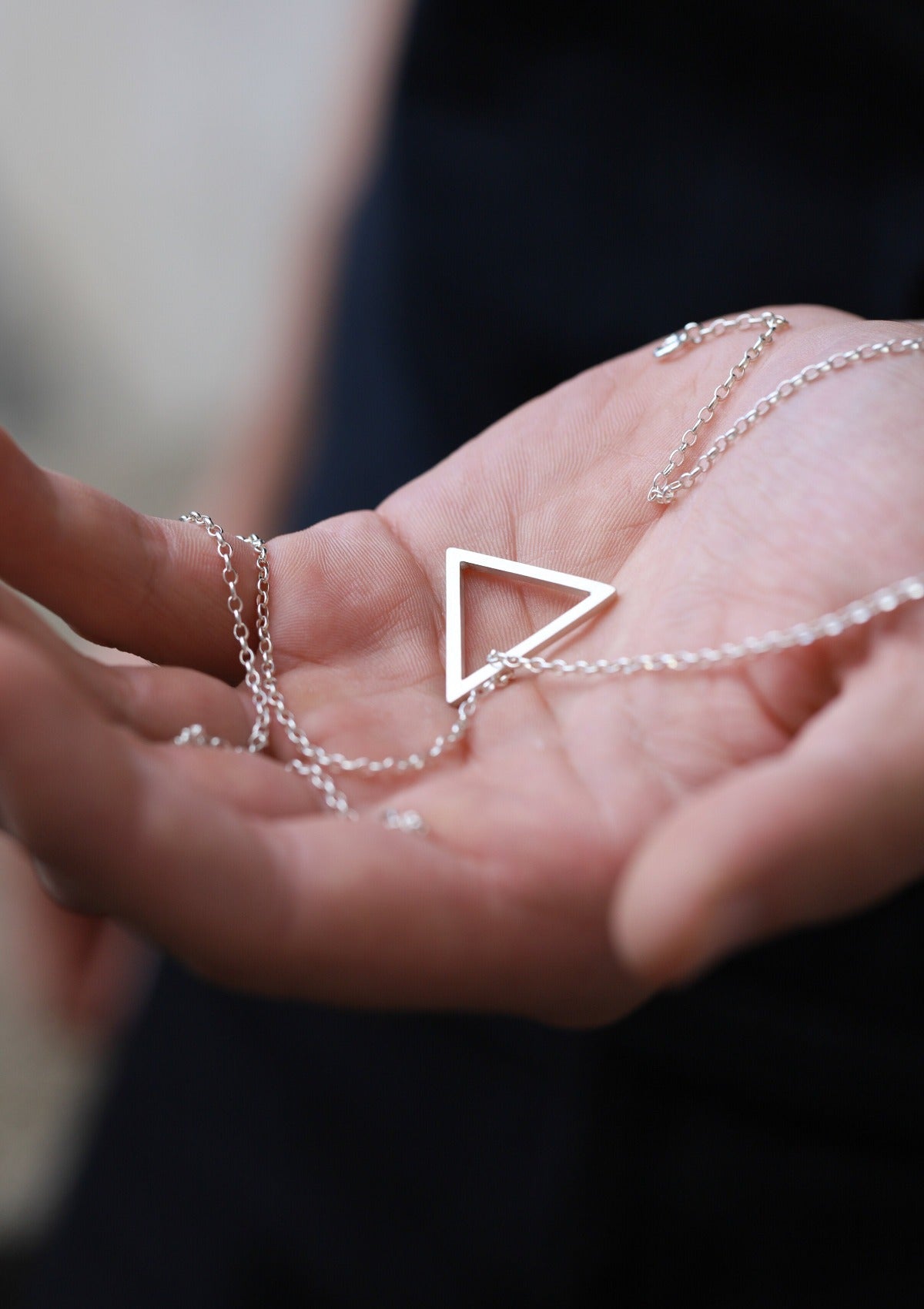 Sterling silver triangle necklace held upright, clean geometric form with modern styling in natural light