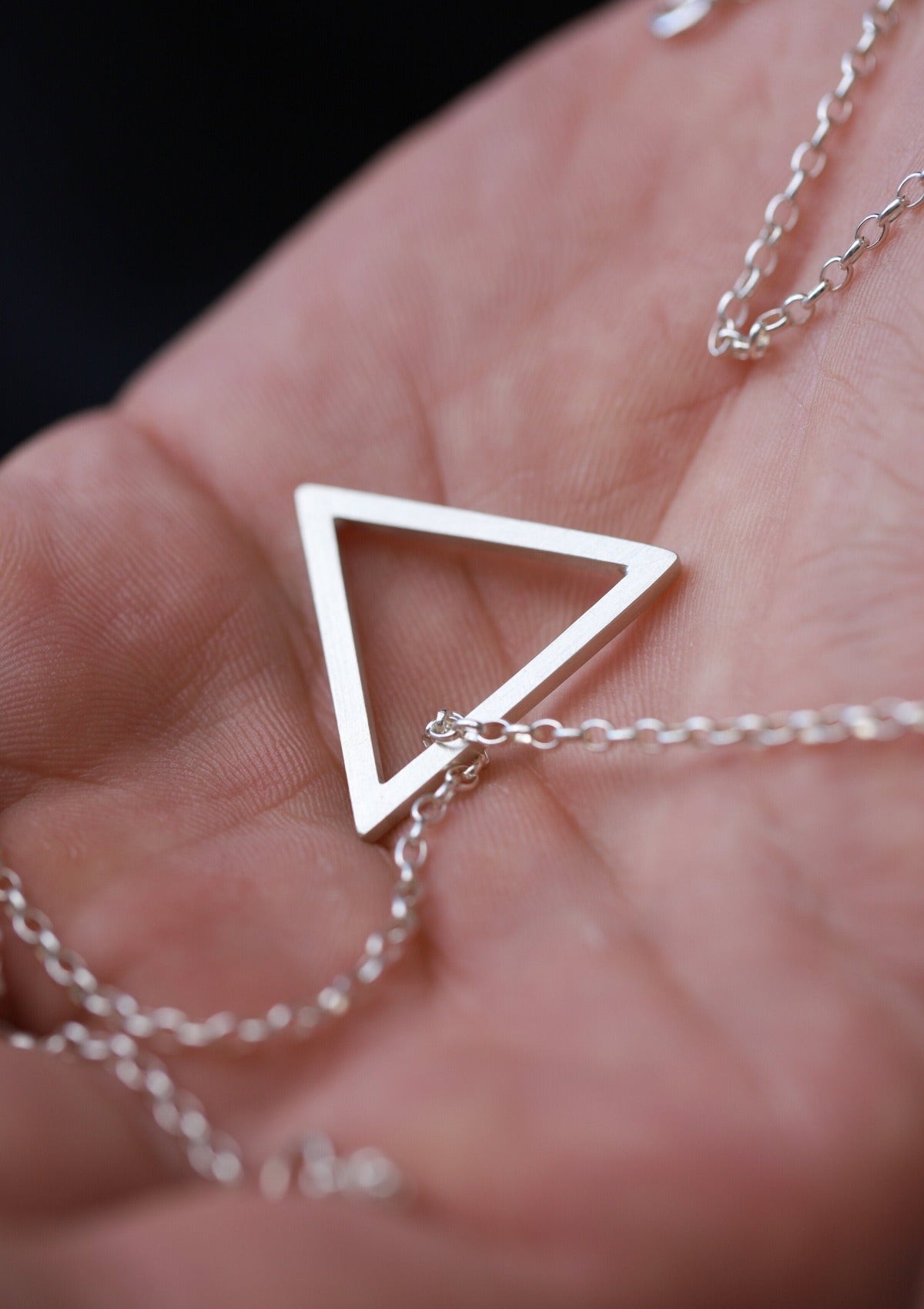 Matte silver triangle pendant displayed in open palm, showcasing scale and minimalist craftsmanship
