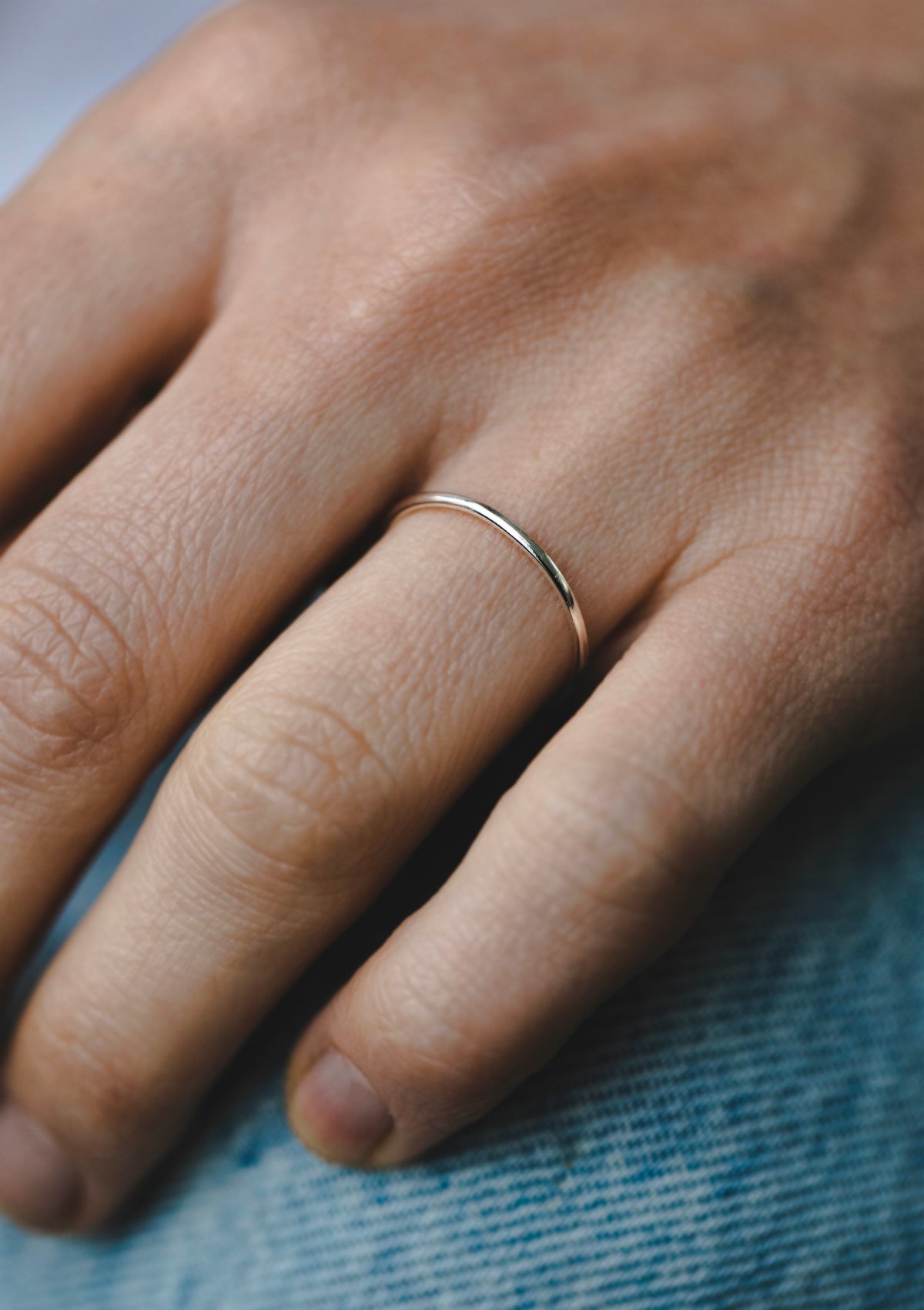 Close-up of shiny sterling silver 1 mm ring worn alone on finger