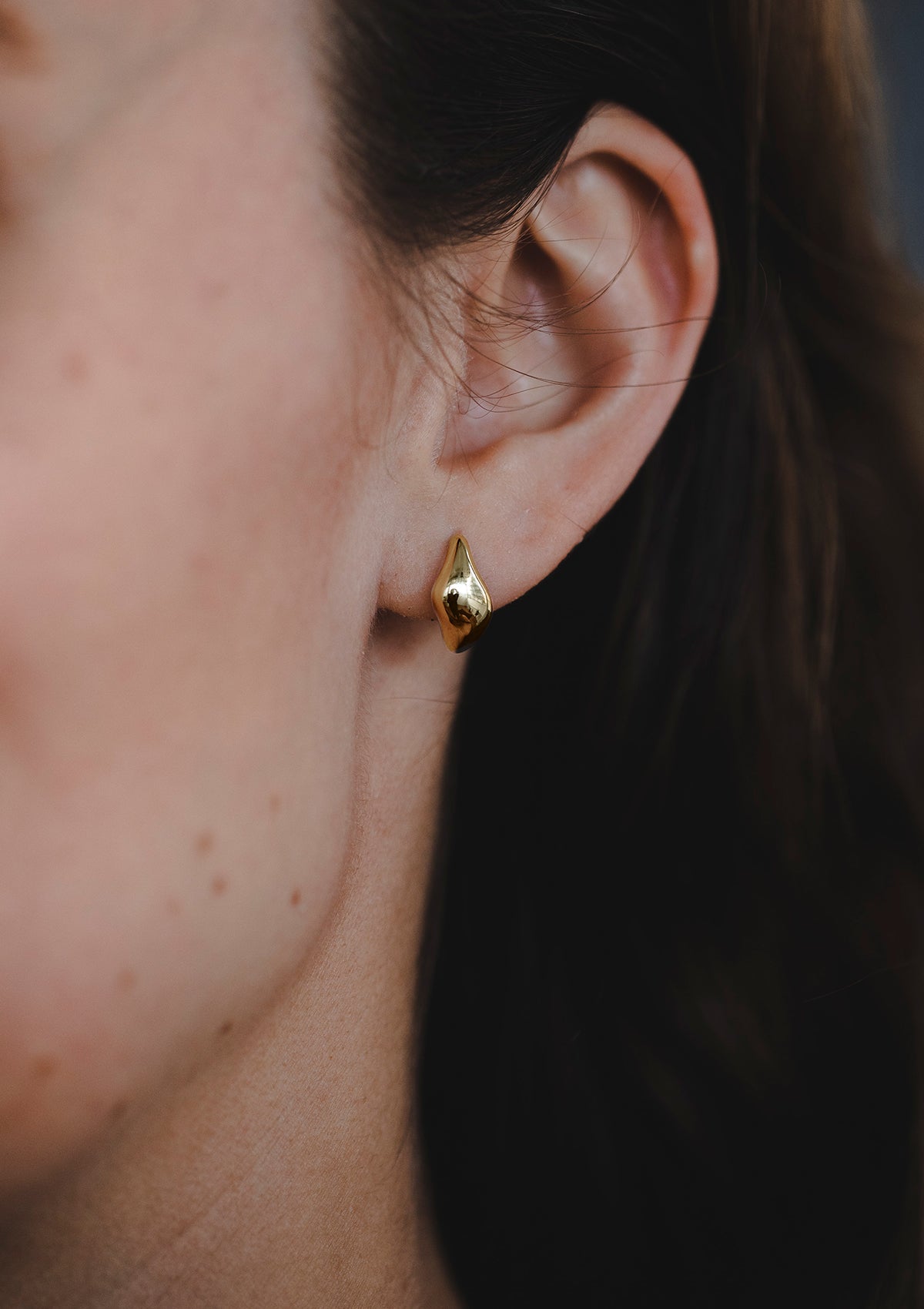 Model wearing minimalist gold huggie earring with wave-inspired curve