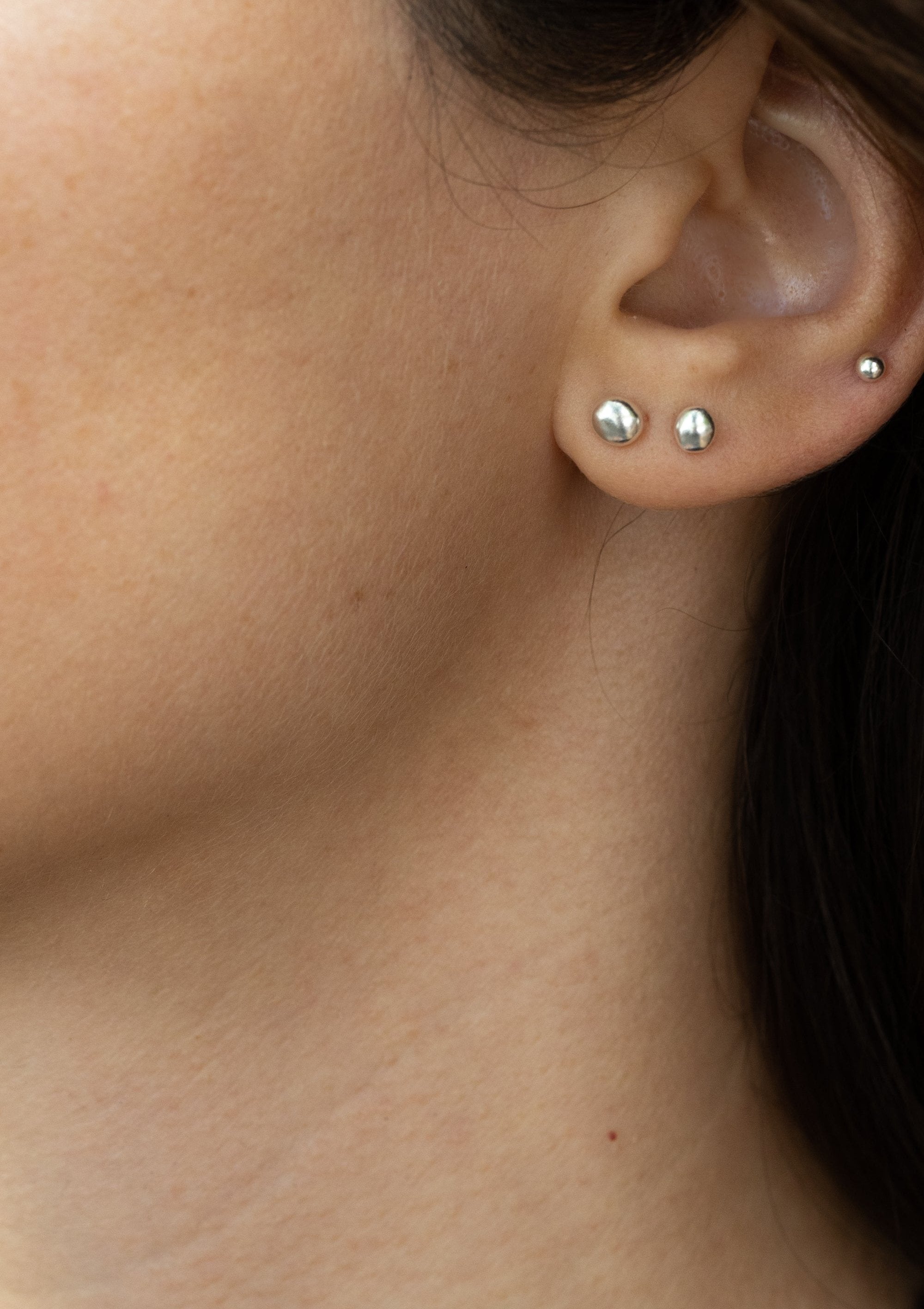 Organic grain-shaped silver earrings worn as mismatched studs, subtle sparkle shown on earlobe