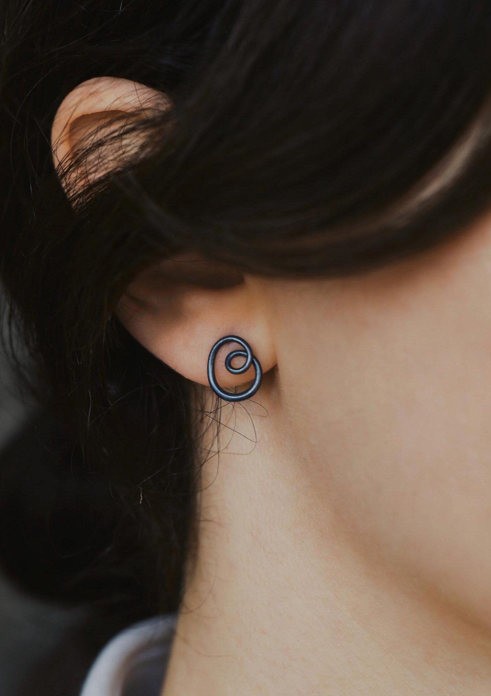 Close-up of an ear wearing a small hoop earring with dark hair.