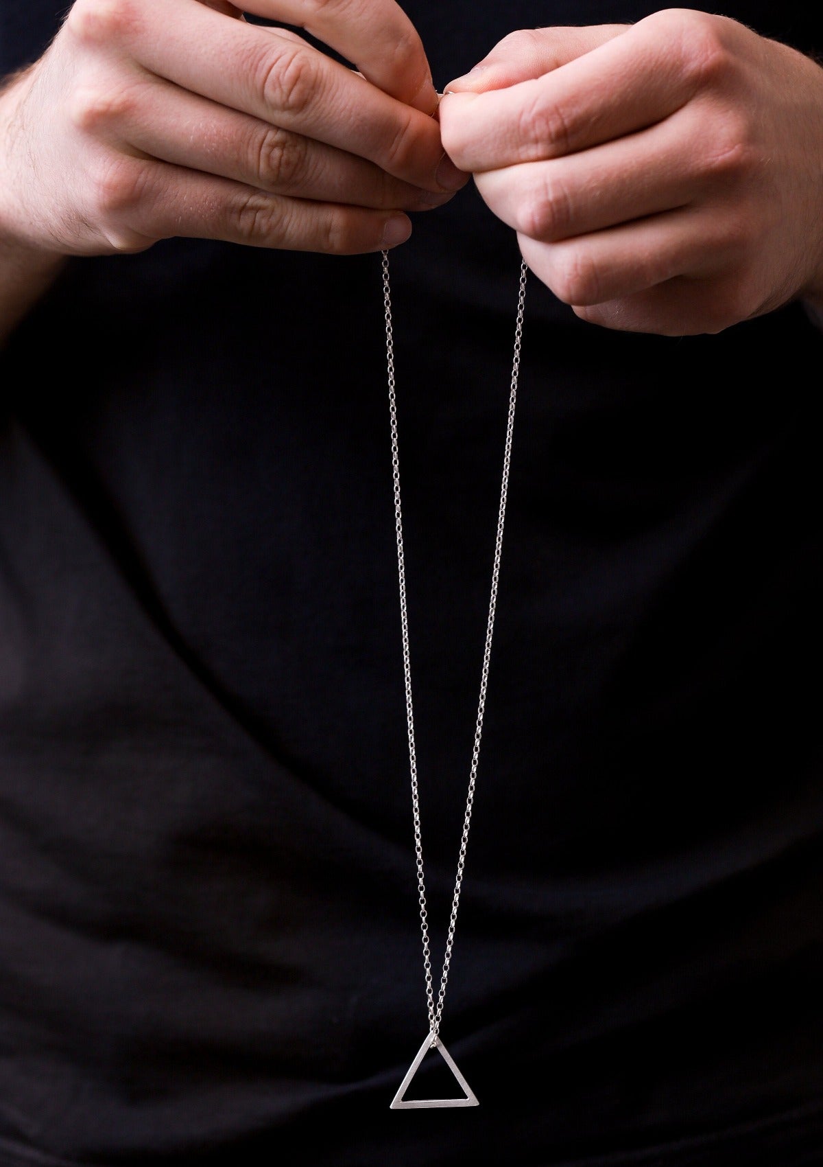 Geometric triangle mens pendant in sterling silver gently hanging from fingers, textured chain in soft focus